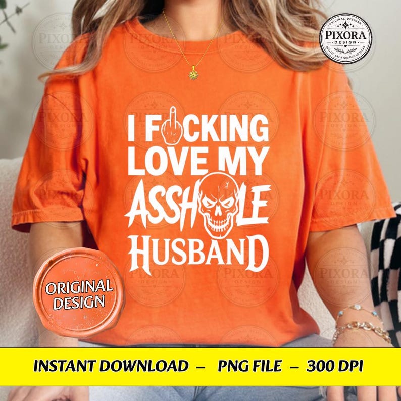 May include: An orange short-sleeved t-shirt featuring white text that reads I FUCKING LOVE MY ASSHOLE HUSBAND with a graphic of a middle finger icon replacing the letter U and a skull illustration replacing the letter O in the word ASSHOLE.