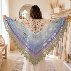 May include: A triangular crochet shawl featuring a gradient color transition from cream at the top to light blue, purple, and ending in a sage green scalloped lace border. The intricate openwork pattern radiates from the center to the edges.