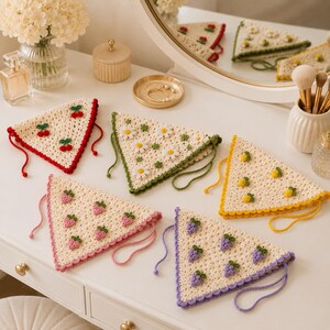 May include: Five triangular crochet headscarves in cream yarn, each featuring a unique motif including red cherries, white daisies, yellow lemons, pink strawberries, and purple grapes, finished with matching colored scalloped edges and ties.