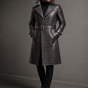 Puede incluir: Una gabardina gris carbón con un patrón de textura de piel de cocodrilo, un cuello de solapa ancho y un cinturón a juego con una hebilla rectangular. El abrigo se lleva sobre un suéter de cuello alto negro, pantalones negros y botas de cuero negro.