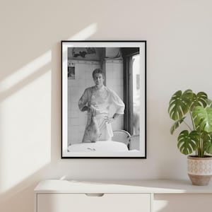 Può includere: Una fotografia incorniciata in bianco e nero che ritrae uno chef in uniforme bianca in piedi in una cucina piastrellata. Lo chef tiene in mano un grosso pezzo di carne cruda sopra un tavolo rotondo. La scena è ripresa in una cucina professionale.