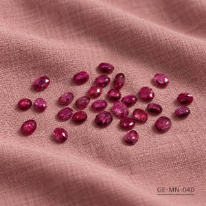Op de afbeelding: Een verzameling kleine, ovaalvormige, gefacetteerde magentakleurige edelstenen verspreid over een roze stof met textuur. De stenen vertonen een diepe, doorschijnende roze tint met meerdere reflecterende oppervlakken. De tekst GE-MN-040 is zichtbaar.