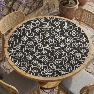 May include: A round table with a light wood frame and a black tabletop featuring a repeating white geometric pattern of interlocking squares and four-petaled floral shapes. The table is surrounded by four matching light wood chairs.