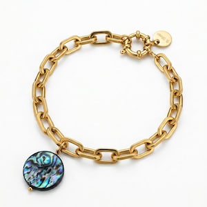 May include: A gold-toned chain link bracelet featuring a round, iridescent abalone shell pendant and a circular spring ring clasp. A small, round metal tag attached to the clasp is engraved with the text S.Steel, indicating the material composition.