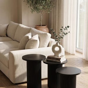 May include: A set of three black side tables with circular tops and fluted cylindrical bases of varying heights. The tables are arranged in a cluster, with the tallest on the left, the medium in the centre, and the shortest on the right side.