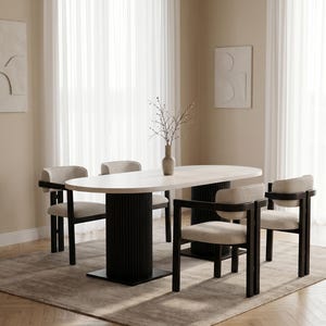 Può includere: Un tavolo da pranzo ovale con piano bianco e due basi cilindriche scanalate nere, accompagnato da quattro sedie con struttura in legno nero e sedute e schienali imbottiti color beige chiaro, con un vaso contenente rami sul tavolo.