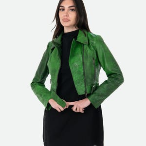 May include: A vibrant green jacket with a textured snakeskin pattern, featuring a notched collar, long sleeves, and a front zip fastening. The jacket is worn over a simple black dress. The design includes silver-toned hardware on the zips.