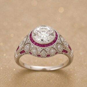 Peut inclure: Une bague argent&eacute;e orn&eacute;e d'une grande pierre centrale ronde et transparente, entour&eacute;e d'un halo de petits rubis rouge fonc&eacute; taill&eacute;s en carr&eacute;. L'anneau et le sertissage pr&eacute;sentent des d&eacute;tails complexes avec de petites pierres blanches.