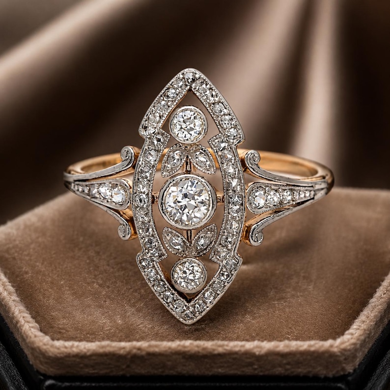 May include: A marquise-shaped ring featuring a central round diamond surrounded by two smaller round diamonds and leaf-shaped accents. The setting is crafted from silver-toned metal with pav&eacute; diamonds, mounted on a polished gold-toned band.