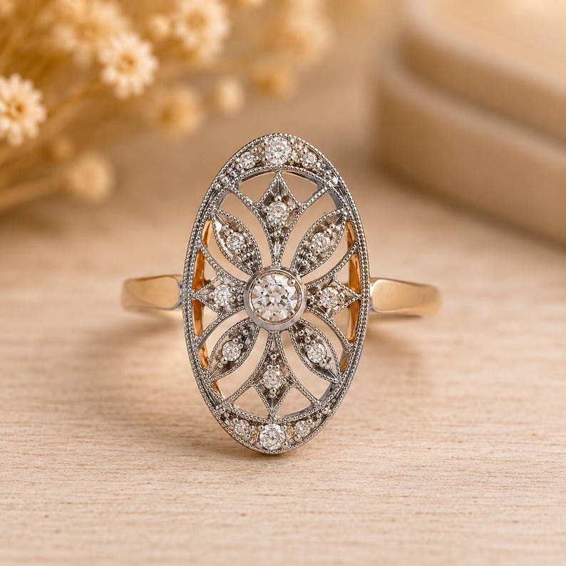 Peut inclure: Une bague de forme ovale avec un diamant rond central entour&eacute; d'une monture en m&eacute;tal filigran&eacute; sertie de plus petits diamants ronds. La bague poss&egrave;de un anneau en or poli reli&eacute; &agrave; la face d&eacute;corative ajour&eacute;e aux tons argent&eacute;s.