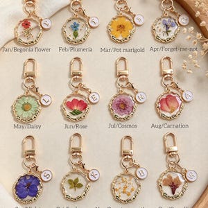 Peut inclure: Douze porte-clés en métal doré avec des pendentifs en résine circulaire contenant des fleurs pressées pour chaque mois : Jan/Bégonia, Fév/Plumeria, Mar/Souci, Avr/Myosotis, Mai/Marguerite, Juin/Rose, Juil/Cosmos, Août/Œillet, Sep/Violette, Oct/Pied-d'alouette, Nov/Osmanthus, Déc/Camélia.