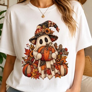 Peut inclure: Un t-shirt blanc avec un motif représentant un fantôme portant un chapeau de sorcière en patchwork, tenant une citrouille et entouré de feuilles d'automne, de tournesols et d'autres citrouilles aux motifs à carreaux et texturés.