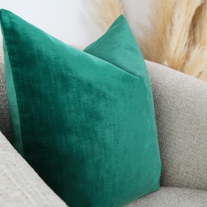 May include: A square throw pillow featuring a solid emerald green velvet fabric cover. The pillow has a smooth, soft-touch texture with a visible sheen characteristic of velvet material, presented in a clean, simple, and structured square shape.