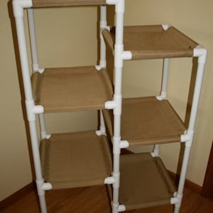 May include: A white PVC pipe cat tree with five platforms covered in brown fabric. The cat tree is freestanding and has a simple design.