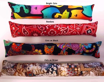 May include: Four cat-themed fabric catnip toys. The toys are long and rectangular, with different patterns. The first toy has a black background with colorful cats and rainbows. The second toy has a red bandana pattern. The third toy has a black background with colorful cats and flowers. The fourth toy has a brown background with cats and flowers.
