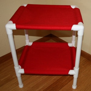 May include: A two-tiered cat bed made of white PVC pipe with red fabric stretched across the top and bottom.