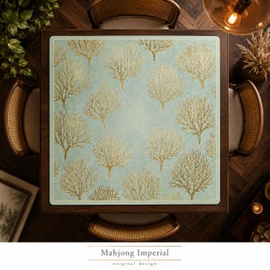 May include: A square mahjong mat featuring a light blue background with a repeating pattern of gold-colored coral-like tree structures. The mat has rounded corners and a thin border, centered on a dark wooden table surrounded by four chairs.
