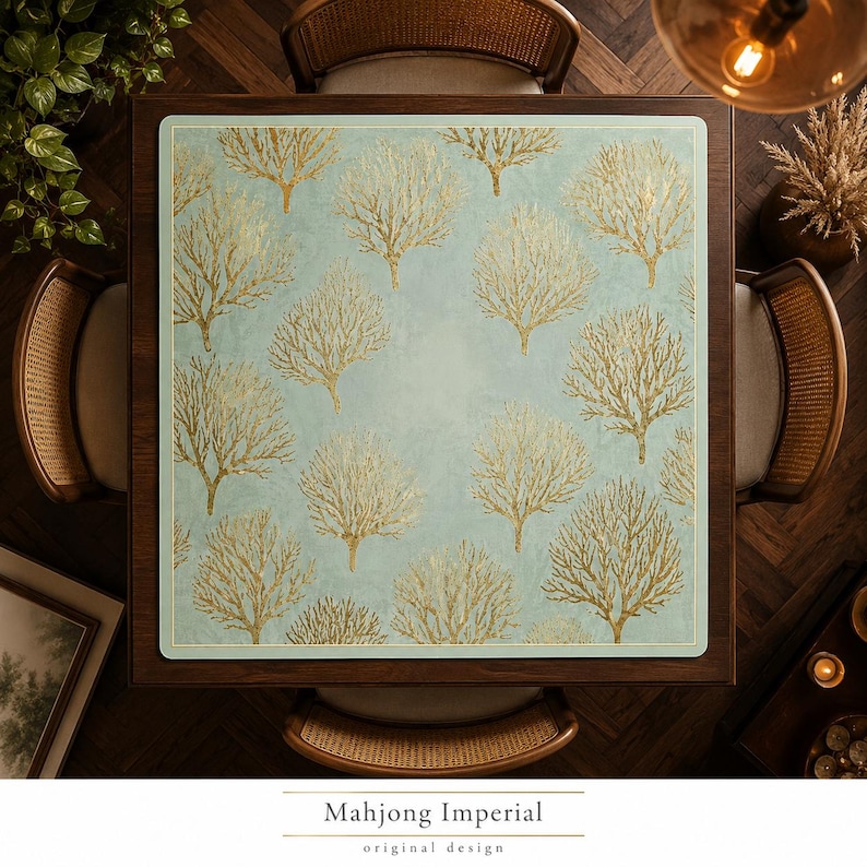 May include: A square mahjong mat featuring a light blue background with a repeating pattern of gold-colored coral-like tree structures. The mat has rounded corners and a thin border, centered on a dark wooden table surrounded by four chairs.