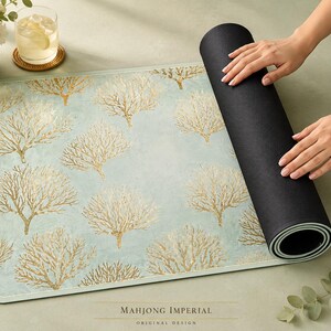 May include: A rectangular mat featuring a light blue background with a repeating gold coral pattern. The mat has a smooth top surface and a solid black underside, partially rolled up to reveal the layered construction and the text Mahjong Imperial.