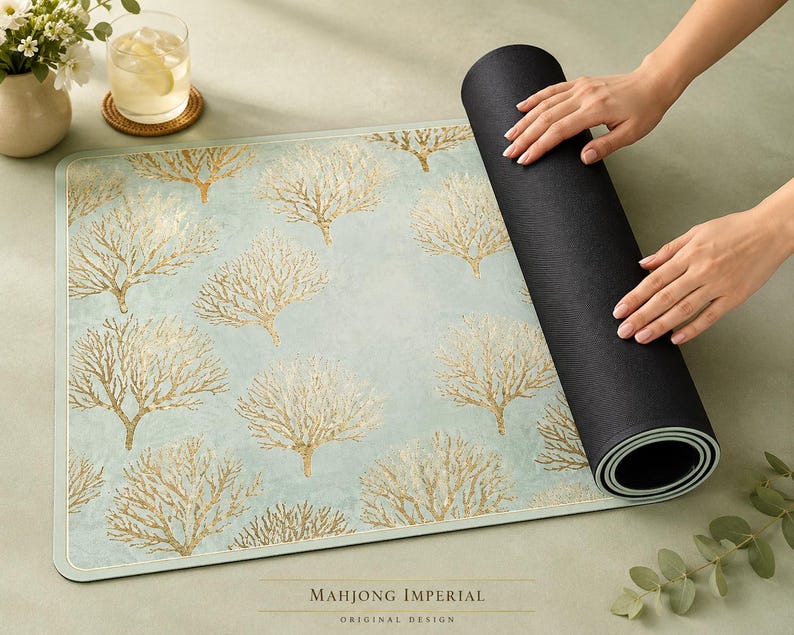 May include: A rectangular mat featuring a light blue background with a repeating gold coral pattern. The mat has a smooth top surface and a solid black underside, partially rolled up to reveal the layered construction and the text Mahjong Imperial.
