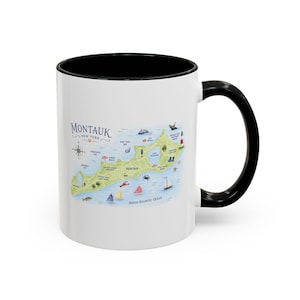 May include: A white ceramic mug with a black rim and handle, featuring a colorful illustrated map of Montauk, New York. The design includes landmarks, nautical icons, and the text Montauk New York printed in blue on the front surface.