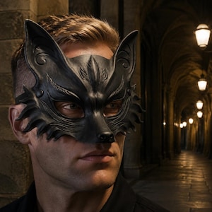 May include: A black fox mask featuring intricate embossed details, pointed ears, and stylized fur textures around the edges. The mask covers the upper portion of the face, including the eyes, and is secured with a strap around the head.