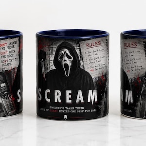 Op de afbeelding: Een keramische mok met een donkerblauwe binnenkant en handvat, voorzien van een rondlopende afbeelding uit de film Scream. Het ontwerp toont het Ghostface-masker, een telefoon en de teksten "What's your favorite scary movie?", "Rules" en "Woodsboro".