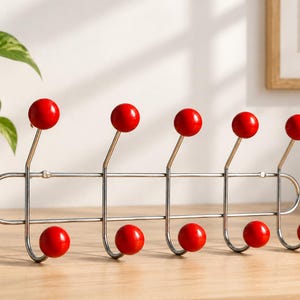 May include: A wall-mounted coat rack featuring a silver-toned metal frame with ten hooks. Each hook is tipped with a smooth, bright red spherical ball. The rack has a horizontal design with five hooks pointing upward and five hooks pointing downward.