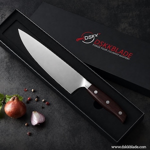 May include: A stainless steel chef knife with a dark brown wooden handle secured by three silver rivets, resting inside a black presentation box labeled with the DSKK logo and the text DSKKBLADE FORGE YOUR CULINARY MASTERY.