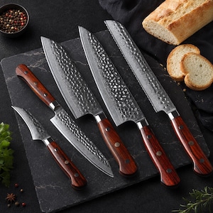May include: A set of four kitchen knives with hammered steel blades and dark wood handles. The blades feature a visible layered pattern and a textured finish. The set includes a small paring knife, two chef knives, and a serrated bread knife.