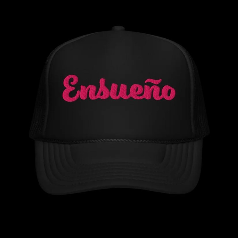 K&ouml;nnte beinhalten: Eine schwarze Trucker-Cap mit strukturierter Vorderseite und Netzr&uuml;ckseite. Das Wort Ensue&ntilde;o ist in einer leuchtend pinken Schreibschrift mittig auf die Vorderseite gestickt. Die Kappe verf&uuml;gt &uuml;ber einen gebogenen Schirm und einen schwarzen Knopf.