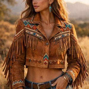 May include: A cropped brown suede jacket featuring long fringe on the sleeves, a notched collar, and intricate multi-colored beadwork in geometric patterns across the shoulders, chest, and cuffs. The jacket is fastened with a single center button.