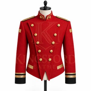 Op de afbeelding: Een rode jas in militaire stijl met een hoge kraag, goudkleurige knopen in een dubbele rij, gouden epauletten op de schouders en zwarte manchetten met gouden biezen. De tekst KINGSFORD LEATHER is zichtbaar in het midden van de jas.
