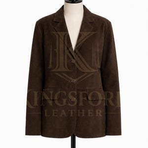 Puede incluir: Una americana de ante marrón oscuro con solapa de muesca, tres botones frontales y dos bolsillos con solapa. La prenda se muestra sobre un maniquí e incluye una marca de agua con el texto KINGSFORD LEATHER centrado en la parte frontal.