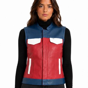 Puede incluir: Un chaleco sin mangas con cuerpo principal rojo, cuello y dobladillo azules, y detalles blancos en los dos bolsillos del pecho y dos bolsillos laterales verticales. La prenda presenta un cuello tipo mao y un cierre central sobre un cuello alto.