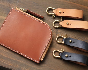 May include: A brown leather zippered wallet with white stitching and three leather keychains with brass rings and snaps. Two keychains are brown leather and one is black leather.