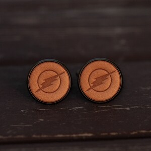 May include: A pair of cufflinks with a brown leather background and a black lightning bolt design.
