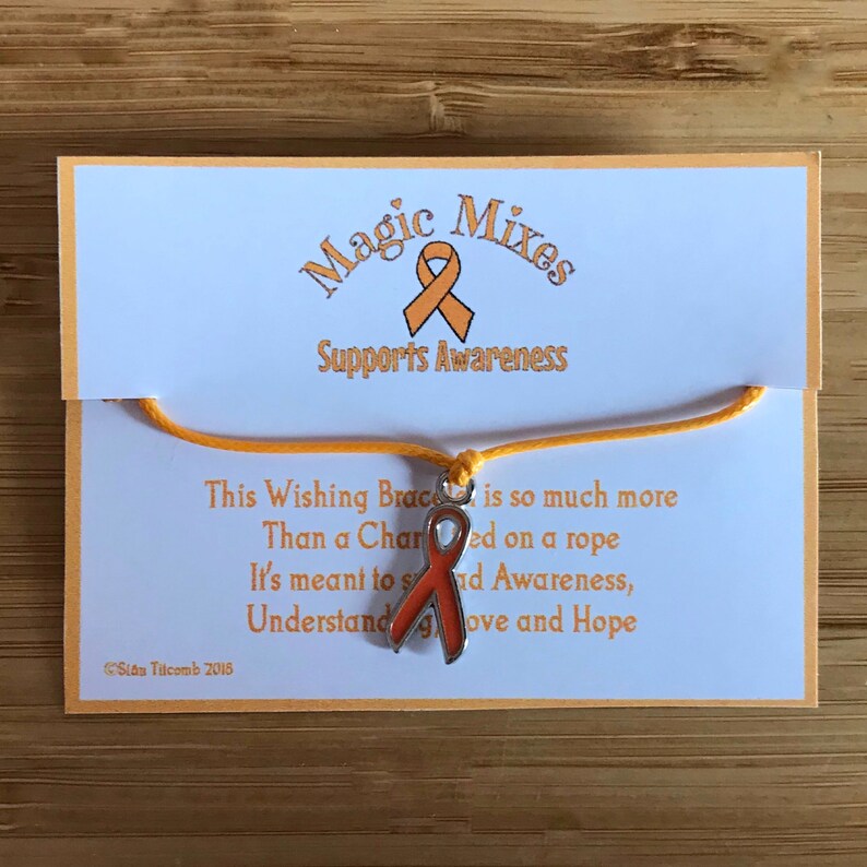 May include: An orange awareness ribbon charm bracelet on a card with the text "Magic Mixes Supports Awareness". The card also includes a poem about the bracelet's meaning. The bracelet is on a wooden surface.
