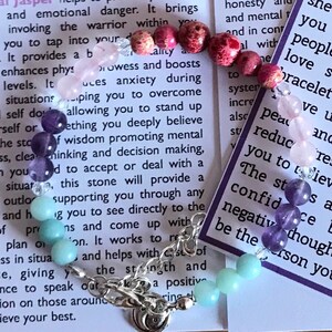 May include: A bracelet made with various colored stones, including amethyst, rose quartz, and aquamarine. The bracelet is on a white background with text about the stones' properties. The text reads: "honesty and mental... peace... reduce... The st... confid... negative though... be the person you..."