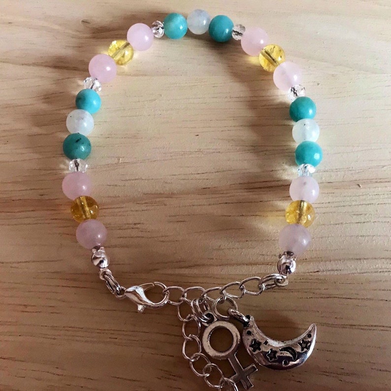 May include: A bracelet made with pink, yellow, and turquoise beads with a silver charm of a crescent moon and a female symbol.