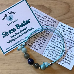 May include: A light blue bracelet with silver beads and various colored gemstones, including blue, green, and aqua. The bracelet is labeled "Stress Buster Gemstone Bracelet Helping to Calm Panic Attacks".