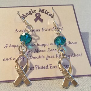 May include: Silver-plated awareness earrings with a teal crystal bead and a ribbon charm that says "HOPE." The earrings are suspended from silver hooks and are displayed on a card with the text "Magic Mixes Awareness Earrings!"