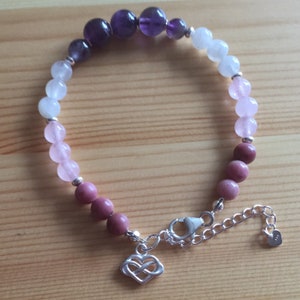 May include: A purple, pink, and white beaded bracelet with a silver infinity heart charm and a silver clasp.