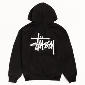 Könnte beinhalten: Ein schwarzer Kapuzenpullover mit einem weißen Stüssy-Logo auf der Rückseite. Das Kleidungsstück verfügt über eine Kapuze, lange Ärmel mit gerippten Bündchen und einen gerippten Saum, wobei der Markenname in einer stilisierten weißen Schrift erscheint.