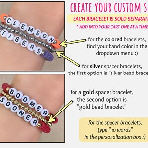 Puede incluir: Primer plano de pulseras de cuentas personalizadas. Una pulsera deletrea "CLEMSON TIGERS" con cuentas de letras blancas y espaciadores plateados. Otra deletrea "BOOMER SOONER" con cuentas de letras blancas y espaciadores dorados. El texto "CREATE YOUR CUSTOM SET!" tambi&eacute;n es visible.