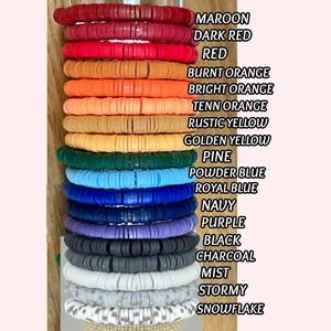 Puede incluir: Una pila de pulseras de cuentas de arcilla coloridas en varios tonos, incluyendo granate, rojo, naranja, amarillo, verde, azul, morado, gris y blanco. Cada pulsera est&aacute; hecha de peque&ntilde;as cuentas redondas y planas. La imagen tambi&eacute;n incluye una lista de los colores.