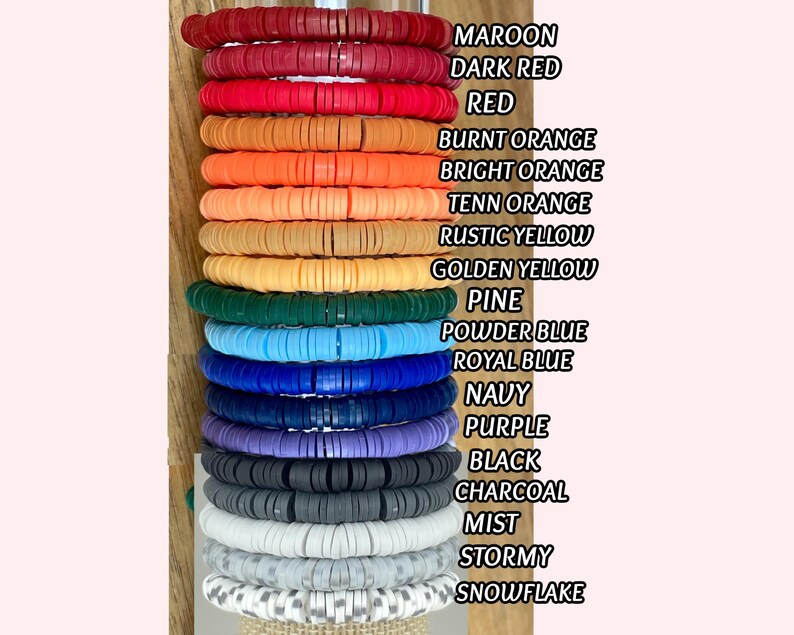 Puede incluir: Una pila de pulseras de cuentas de arcilla coloridas en varios tonos, incluyendo granate, rojo, naranja, amarillo, verde, azul, morado, gris y blanco. Cada pulsera est&aacute; hecha de peque&ntilde;as cuentas redondas y planas. La imagen tambi&eacute;n incluye una lista de los colores.