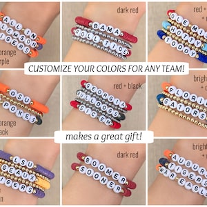Puede incluir: Una colecci&oacute;n de pulseras de cuentas en varios colores de equipo, con nombres y frases de equipo. Las pulseras incluyen cuentas de color naranja brillante, morado, rojo, negro, azul y dorado. El texto de la imagen dice "CUSTOMIZE YOUR COLORS FOR ANY TEAM!" y "makes a great gift!"