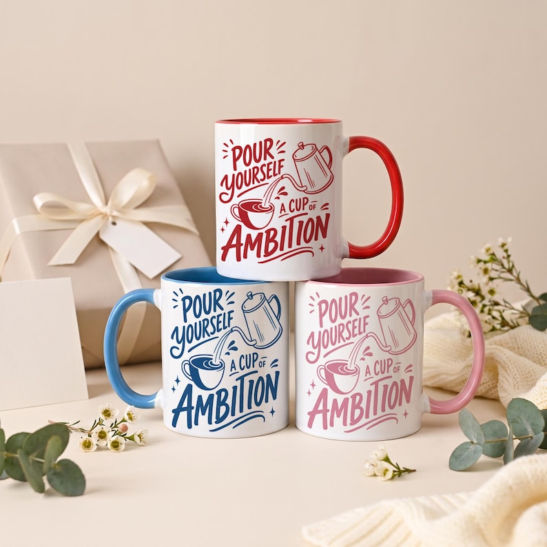 May include: Three ceramic mugs featuring the text "Pour Yourself a Cup of Ambition" with a graphic of a coffee pot pouring into a cup. One mug has a red handle and interior, one has a blue handle and interior, and one has a pink handle and interior.