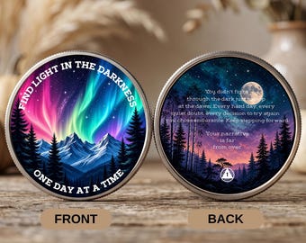 May include: Two circular metal tokens with serrated edges. The left token shows a mountain range under a colorful aurora borealis with the text FIND LIGHT IN THE DARKNESS ONE DAY AT A TIME. The right token features a moonlit forest and text.